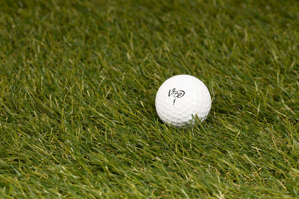 A serene golf course at sunrise with various grades of golf balls on lush green grass and personalized golf accessories in the background.